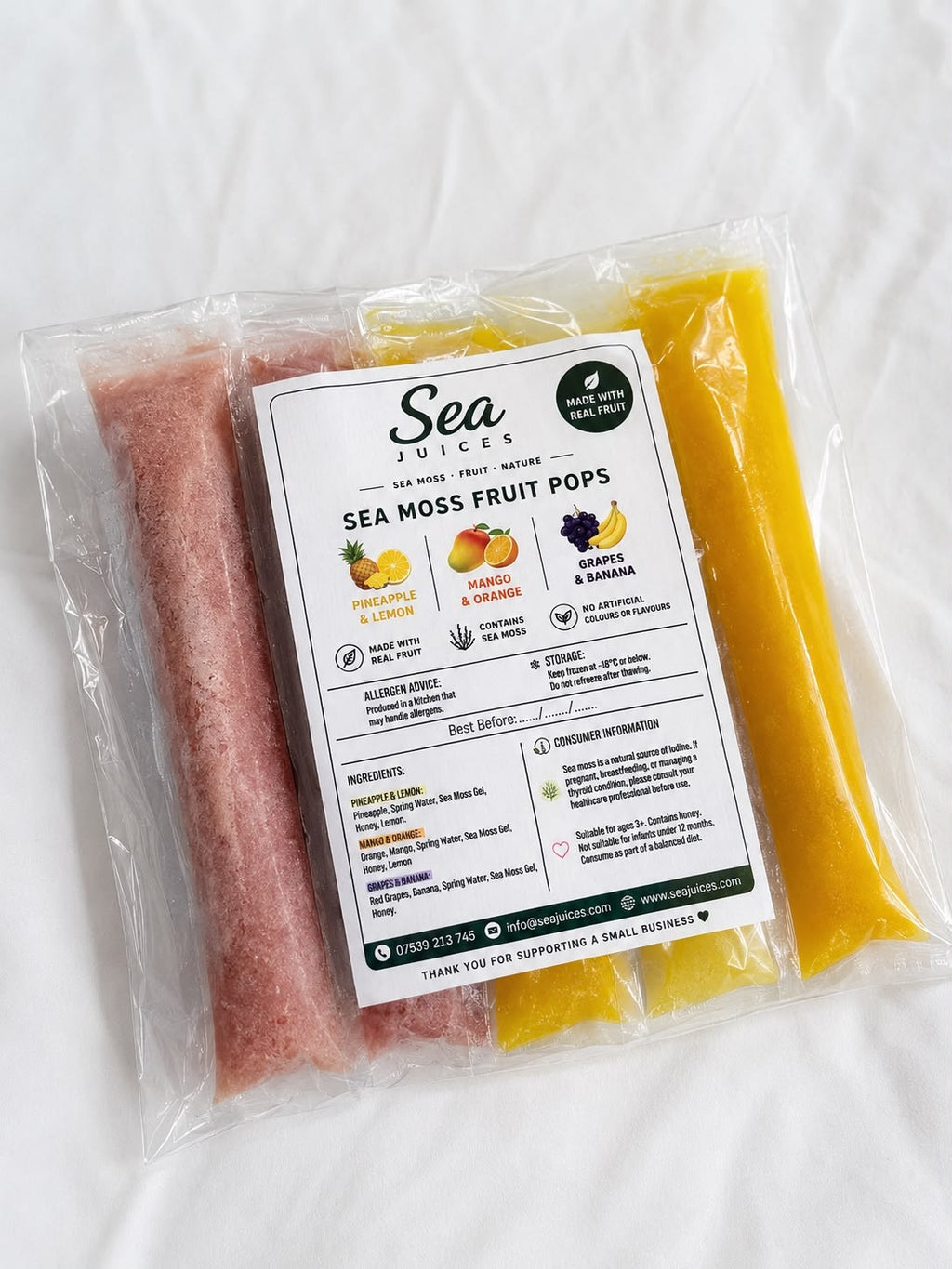 A packaged bag of Sea Juices Sea Moss Fruit Pops, showing pink and yellow pouches inside clear plastic packaging with a detailed white product label, set on a white fabric background.