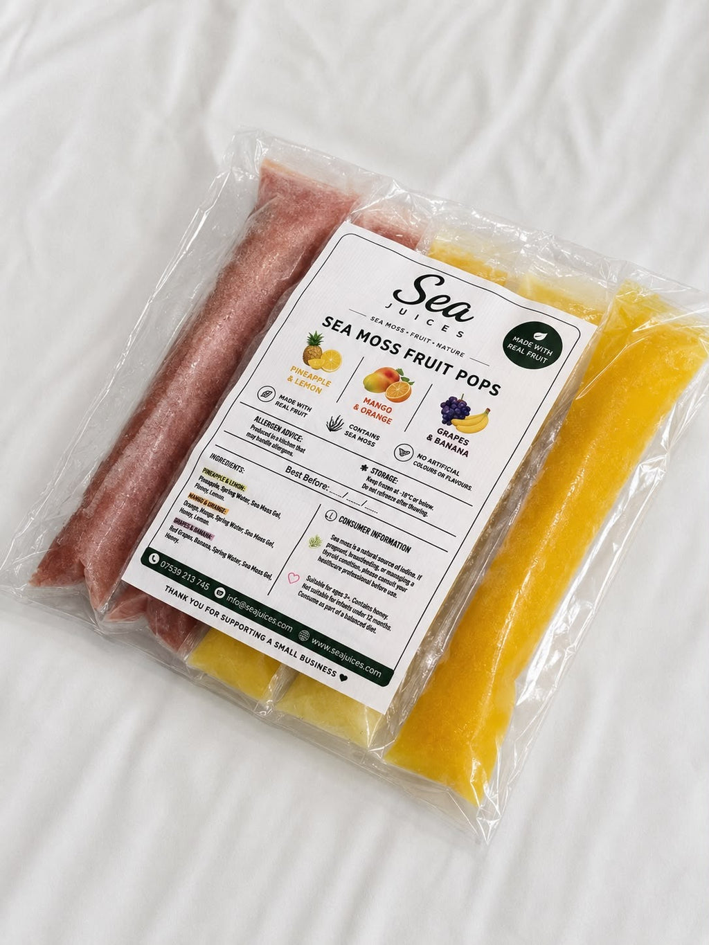 A clear plastic bag of Sea Snacks Sea Moss Fruit Pops, showing two long strips of frozen popsicles inside: one pinkish-red and one bright yellow. A white paper label with product details is centered on the front.